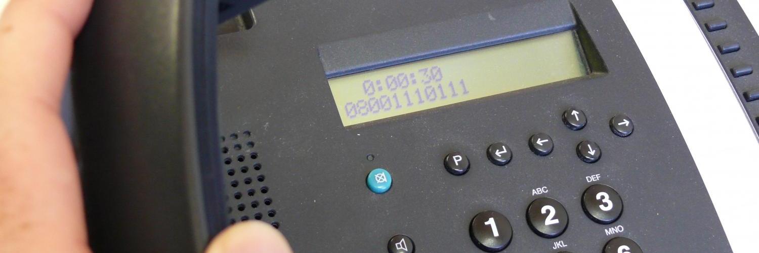 Hand hält Hörer eines schwarzen Bürotelefons mit Display.