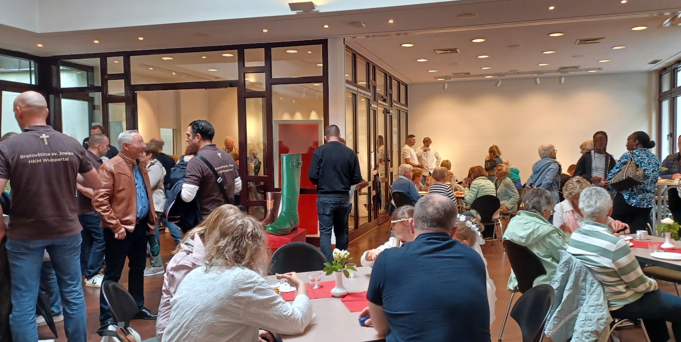 Menschen feiern in einem Saal an Tischen und Stehtischen mit Getränken und Fingerfood