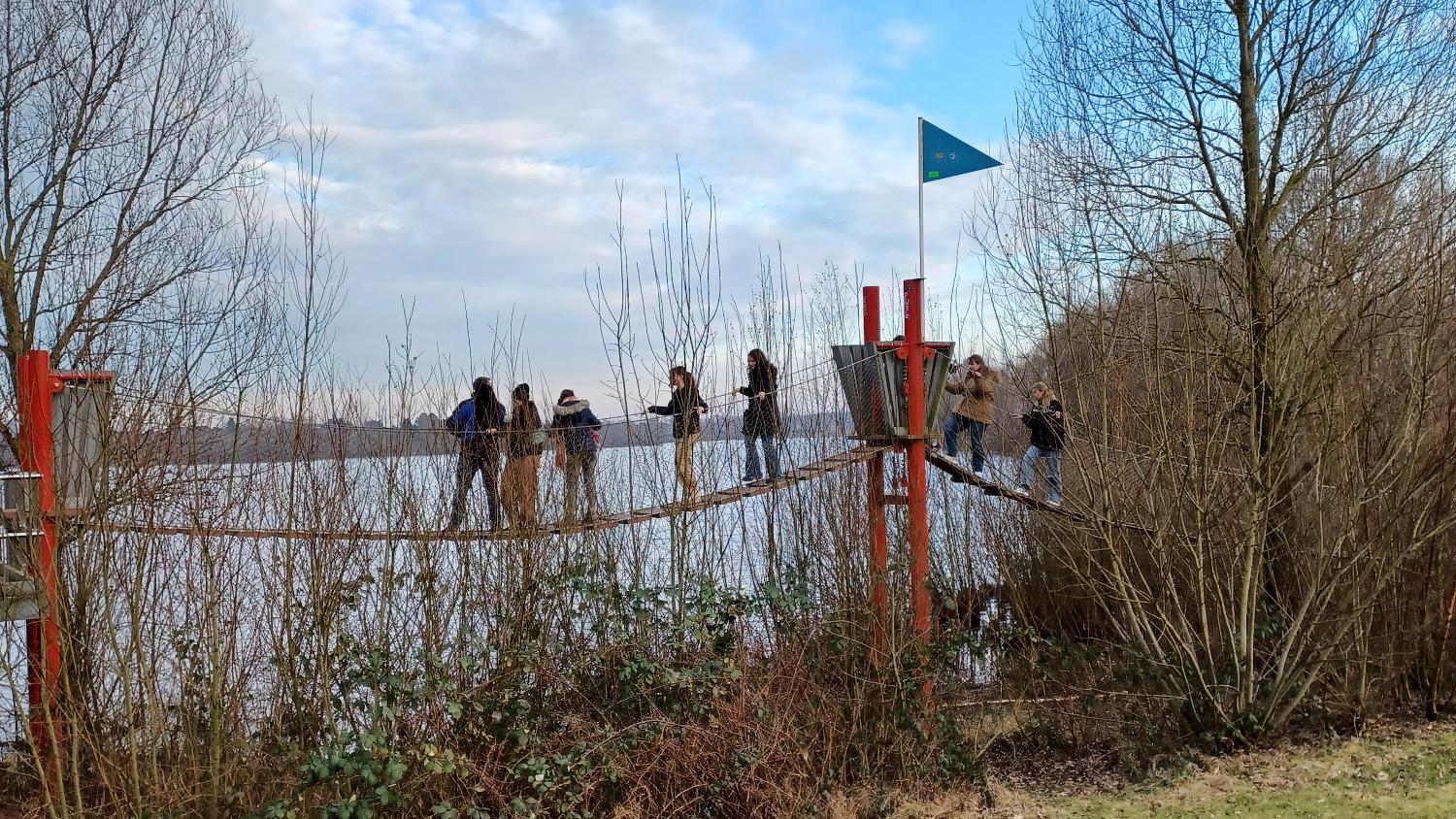 Glaubenskurse Mehrere Personen auf einer Hängebrücke vor einem See