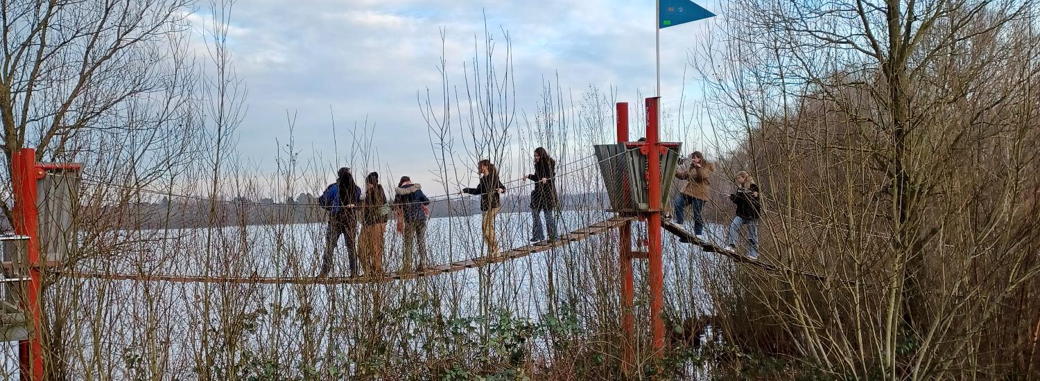 Mehrere Personen auf einer Hängebrücke vor einem See