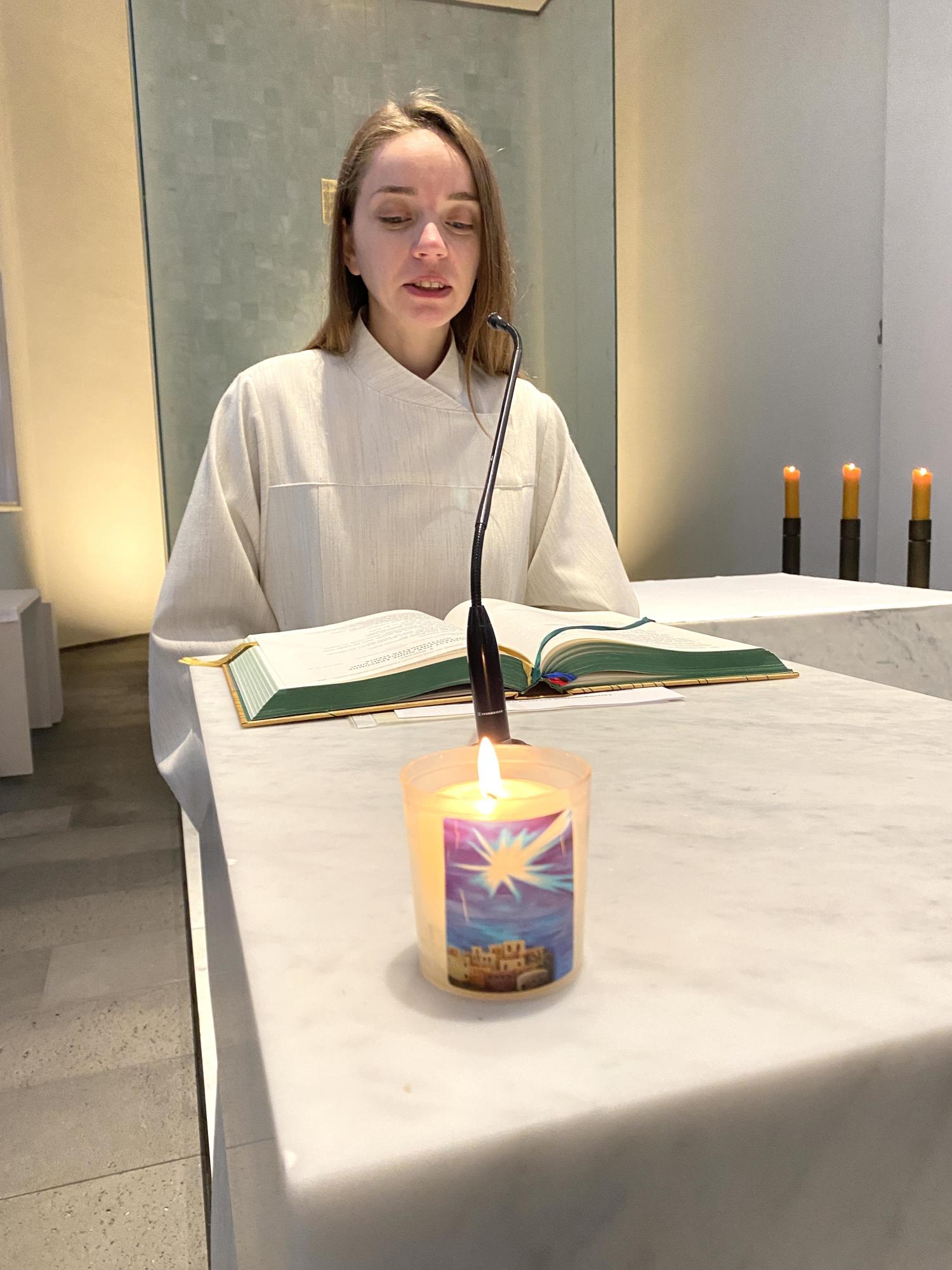 Wortgottesdienstleiterin liest an einem Altar mit Kerze und aufgeschlagenem Evangeliar.