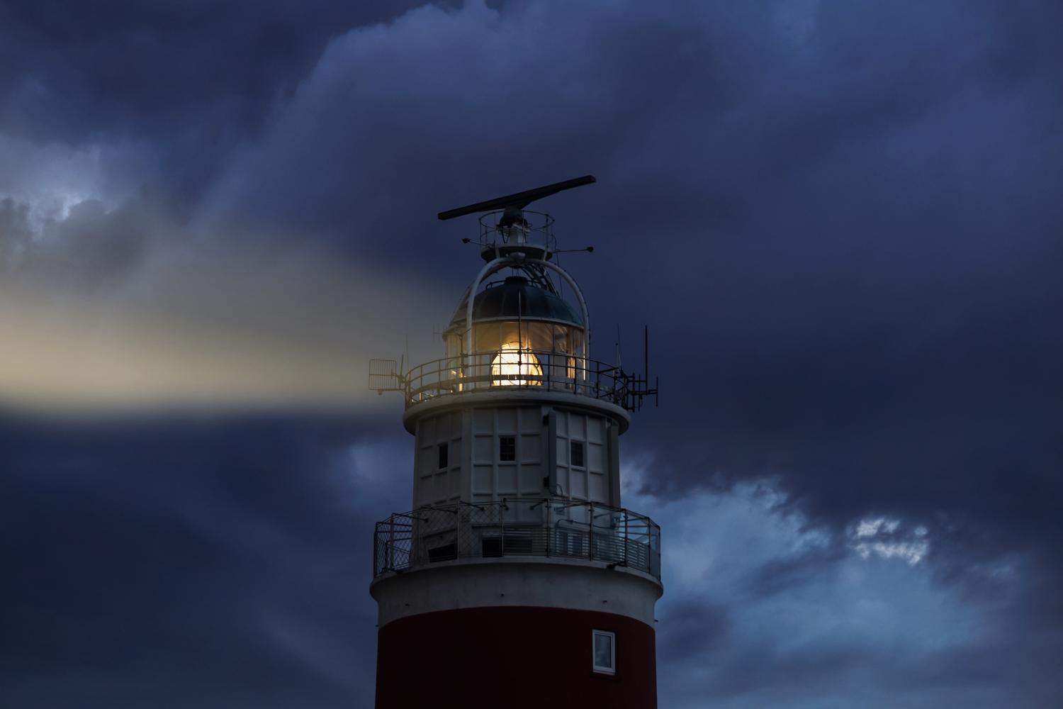 Leuchtturm strahlt Licht in dunkler, wolkiger Nacht.