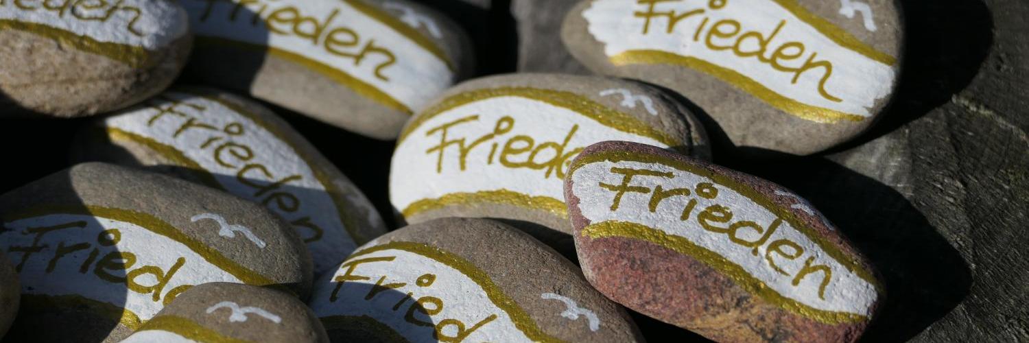Bemalte Steine mit dem Wort „Frieden“ auf Holzuntergrund.