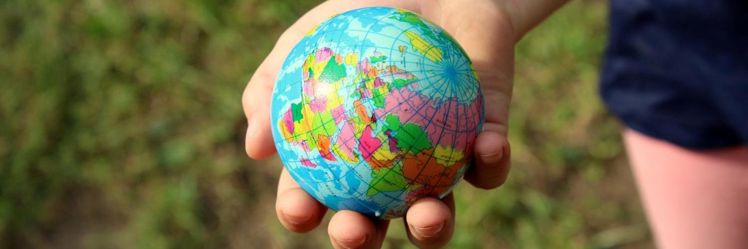 Kinderhand hält kleinen, bunten Globus im Freien.