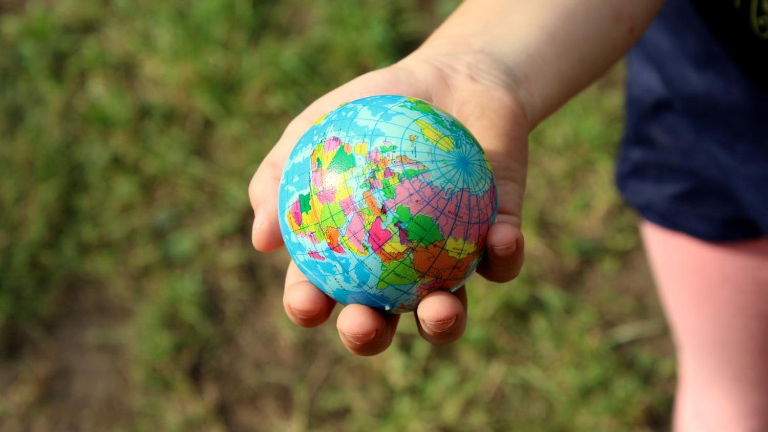Kinderhand hält kleinen, bunten Globus im Freien.