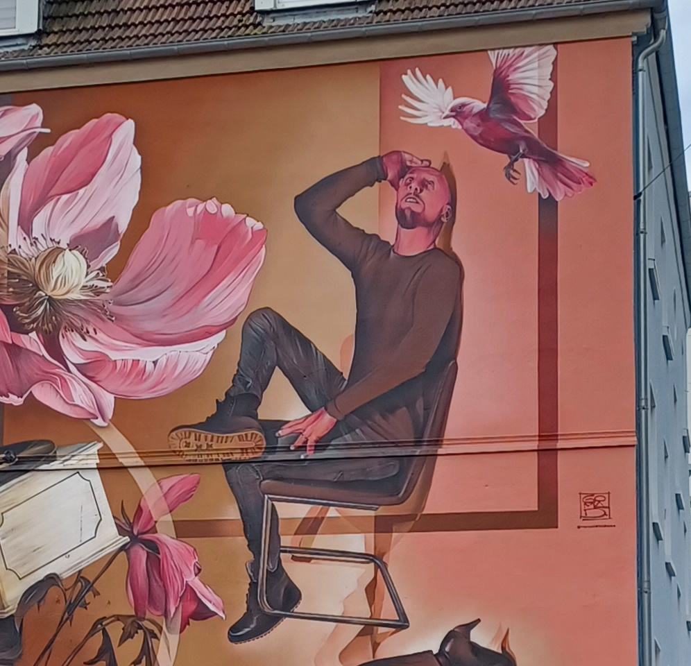 Hauswandbild mit Mann auf einem Stuhl und Vogel