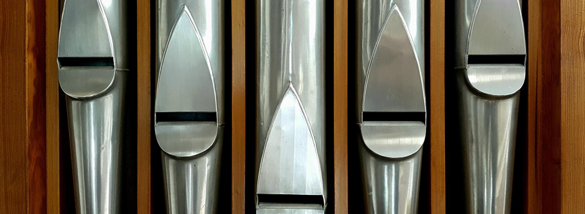 Nahaufnahme von glänzenden Orgelpfeifen aus Metall, von Holz eingerahmt.
